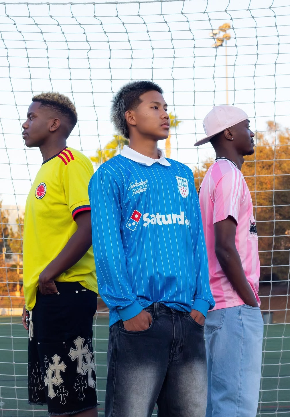 Three soccer players standing back-to-back in front of a goal net